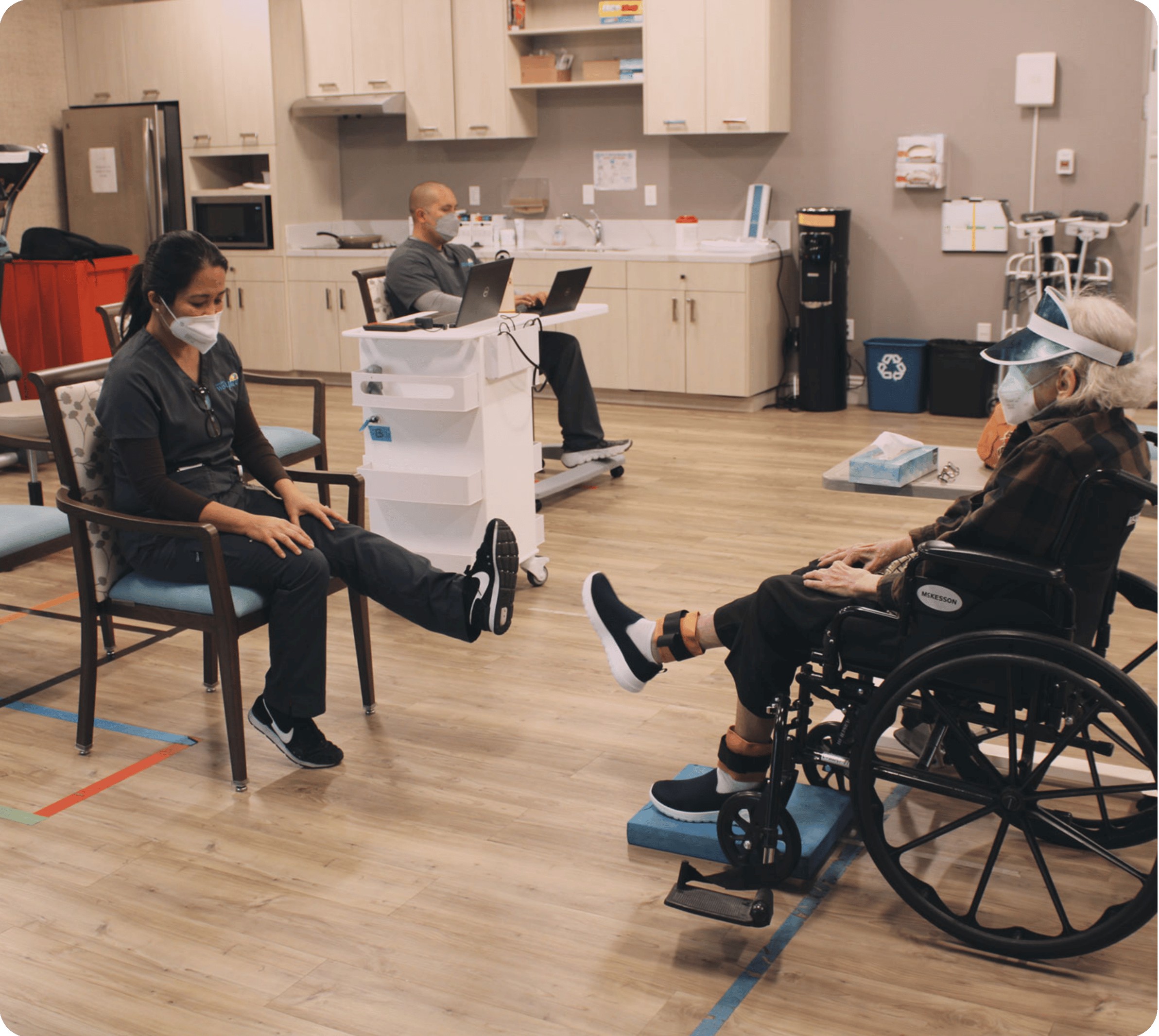 Physical therapist showing elderly woman in a wheelchair how to do her exercises.
